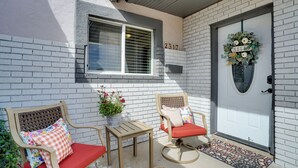A front porch with two wicker chairs, a small table, and a potted plant. A door with a wreath and a mailbox with the number 2317 is visible. - Chic Silver City Getaway w/ Patio + Gas Grill (Silver City)