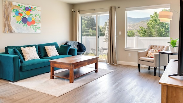 Sala de estar com um sofá azul-turquesa, uma mesa de centro de madeira e vista para uma varanda com montanhas ao fundo.