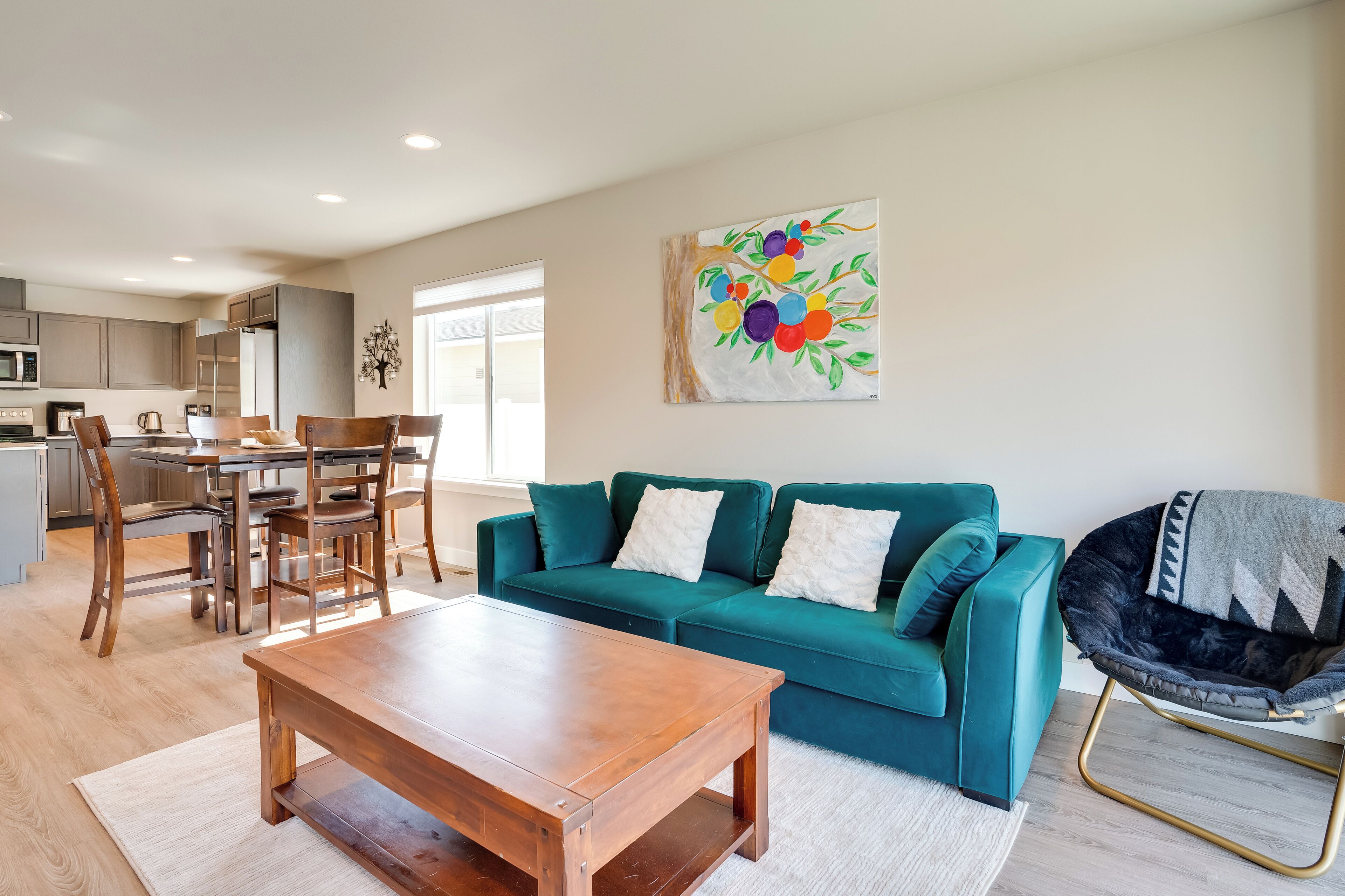 A modern living room with a teal sofa, wooden coffee table, and a colorful fruit painting on the wall.