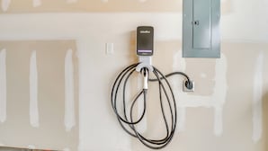 Uma estação de carregamento JuiceBox fixada numa parede, com tomadas elétricas e uma porta visíveis.