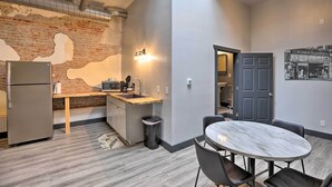 Une cuisine compacte avec un mur en briques, un réfrigérateur, un évier et un petit coin repas comprenant une table et des chaises.