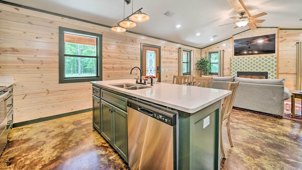A modern kitchen with a dishwasher, a dining area with a table and chairs, and a living room with a sofa and a TV. - Quiet & Peaceful Hochatown Cabin w/ Hot Tub! (Broken Bow)