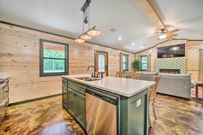 A modern kitchen with a dishwasher, a dining area with a table and chairs, and a living room with a sofa and a TV. - Quiet & Peaceful Hochatown Cabin w/ Hot Tub! (Broken Bow)