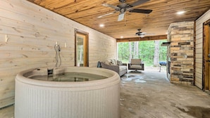 A spa area with a hot tub, wooden ceiling, stone wall, and a view of the forest. - Quiet & Peaceful Hochatown Cabin w/ Hot Tub! (Broken Bow)