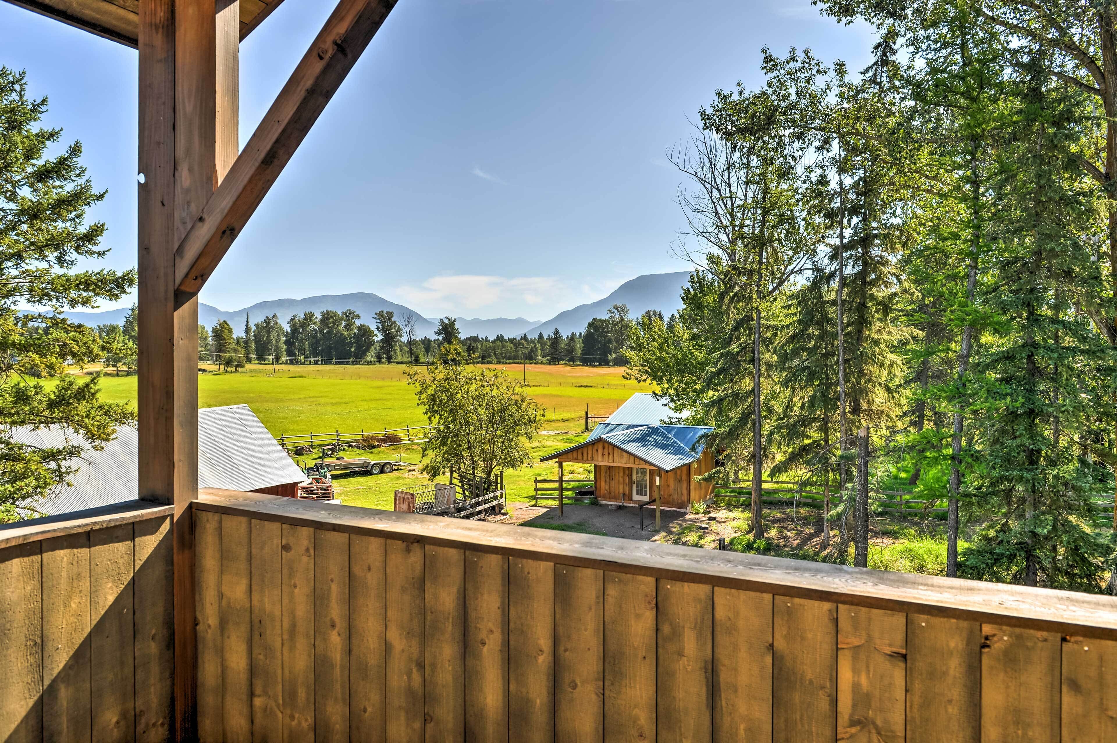 A wooden balcony overlooking a green field and a small cabin.