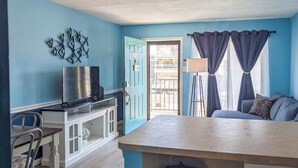 A room with a blue wall, a TV on a white cabinet, a door with the number 205, a window with curtains, and a sofa with pillows. - Coastal Condo w/ Pool, 1 Block to Wildwood Beach! (North Wildwood)