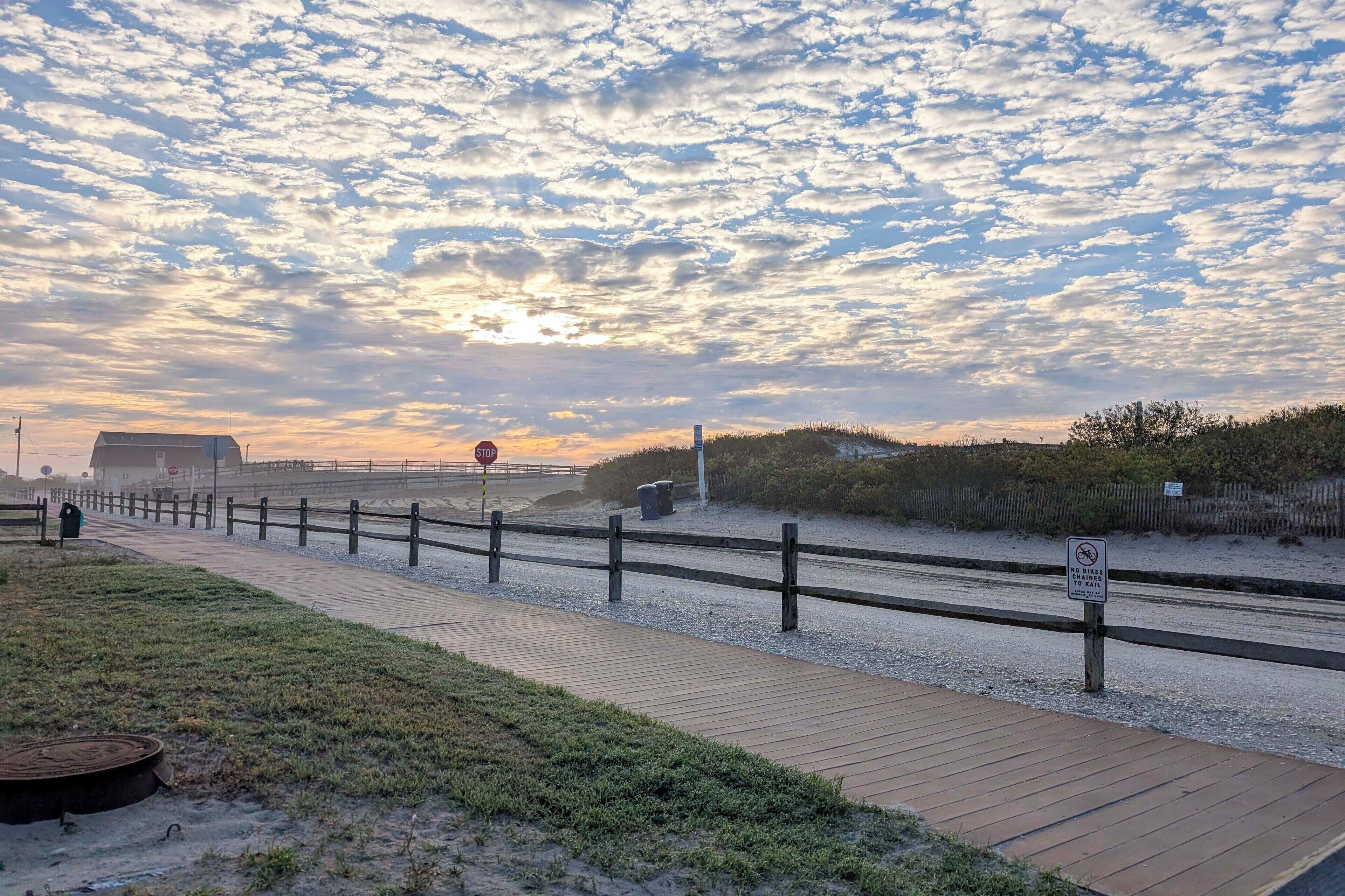 A boardwalk with a stop sign, a no diving sign, and a sandy beach area.