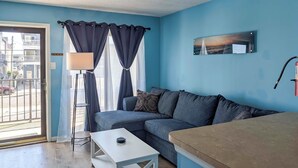 A room with a blue wall, a sofa, a white table, a lamp, and a painting. - Coastal Condo w/ Pool, 1 Block to Wildwood Beach! (North Wildwood)