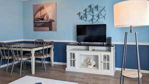 A room with a dining table, chairs, a TV, a cabinet, and a floor lamp. - Coastal Condo w/ Pool, 1 Block to Wildwood Beach! (North Wildwood)