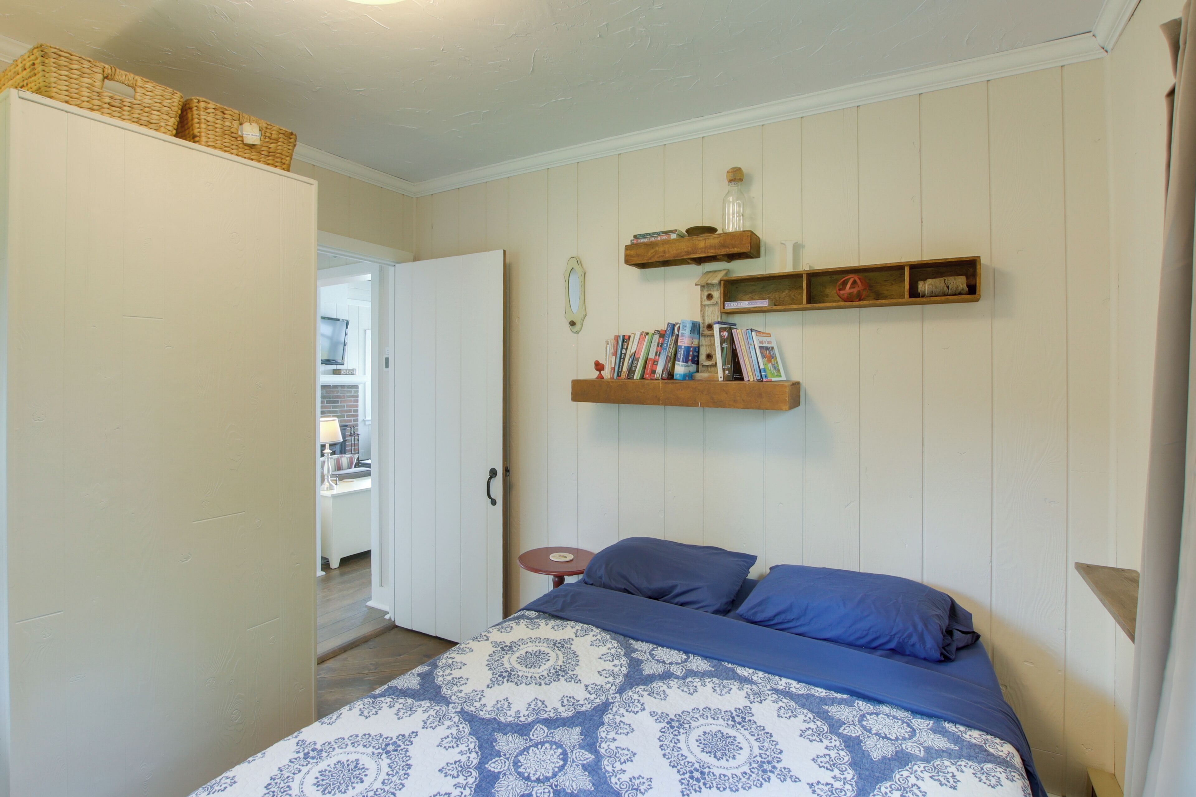 A bedroom with a bed, a wardrobe, and shelves with books and decorative items.