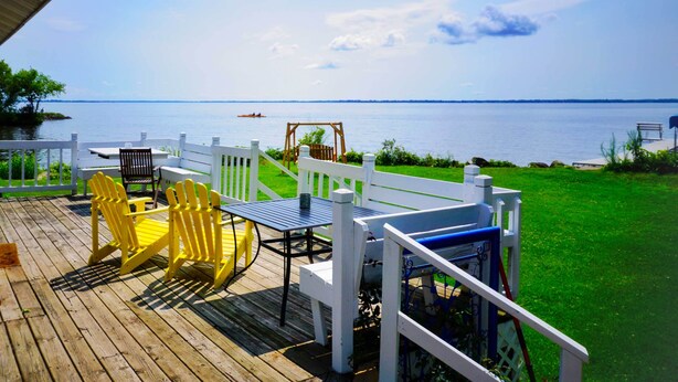 Una terraza de madera con mobiliario exterior, una cerca blanca y vista al agua.