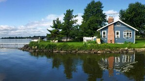 Una casa junto a un lago tranquilo con un muelle, rodeada de árboles y un césped.