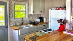 Una cocina con encimera de madera, armarios blancos, un ventanal y un refrigerador.