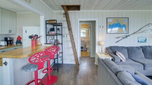 Una cocina con mostrador de madera, taburetes rojos y una escalera que lleva a un altillo.