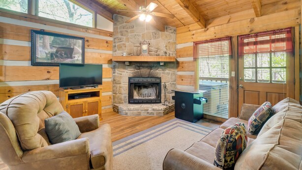A cozy cabin interior with a stone fireplace, wooden walls, a television, and a comfortable seating area. - Covered Deck & Hot Tub: Cozy Gatlinburg Cabin (Gatlinburg)