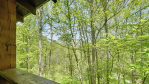 A wooden deck overlooking a dense forest. - Covered Deck & Hot Tub: Cozy Gatlinburg Cabin (Gatlinburg)