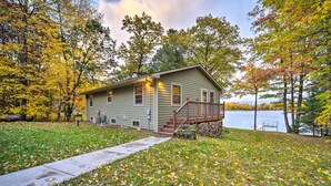 A single-story cabin with a front porch, a small deck, and a pathway leading to the entrance. - Cozy Hayward Cottage w/ Dock & Lakefront View (Hayward)