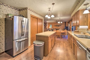 A kitchen with wooden cabinets, a stainless steel refrigerator, a wooden dining table with chairs, and a trash can. - Cozy Hayward Cottage w/ Dock & Lakefront View (Hayward)
