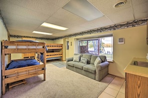 A room with bunk beds, a sofa, a window, and a kitchenette. - Cozy Hayward Cottage w/ Dock & Lakefront View (Hayward)