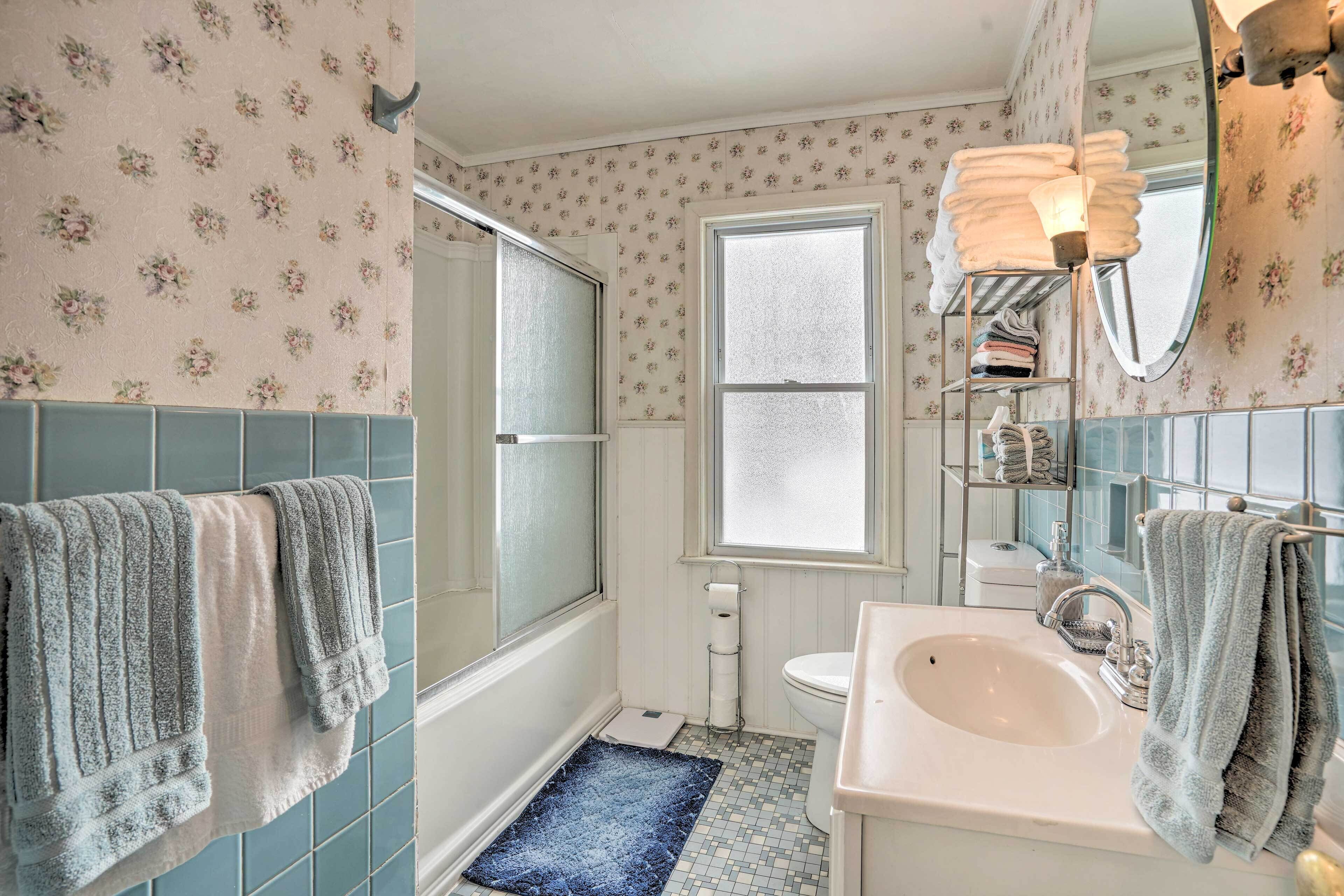 A bathroom with a white sink, a mirror, a towel rack, a window, and a shower area.