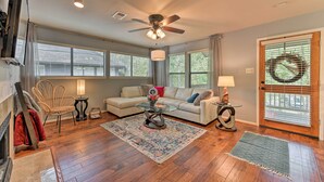 A spacious living room with hardwood floors, a ceiling fan, a glass coffee table, a beige sofa, and a large window providing natural light.
