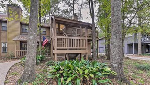 A wooden deck with a staircase leading to a second floor, surrounded by trees and a small garden area.