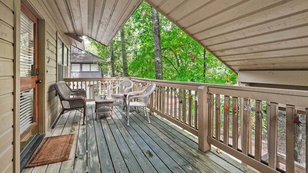 A wooden deck with a railing, a door, and two wicker chairs.