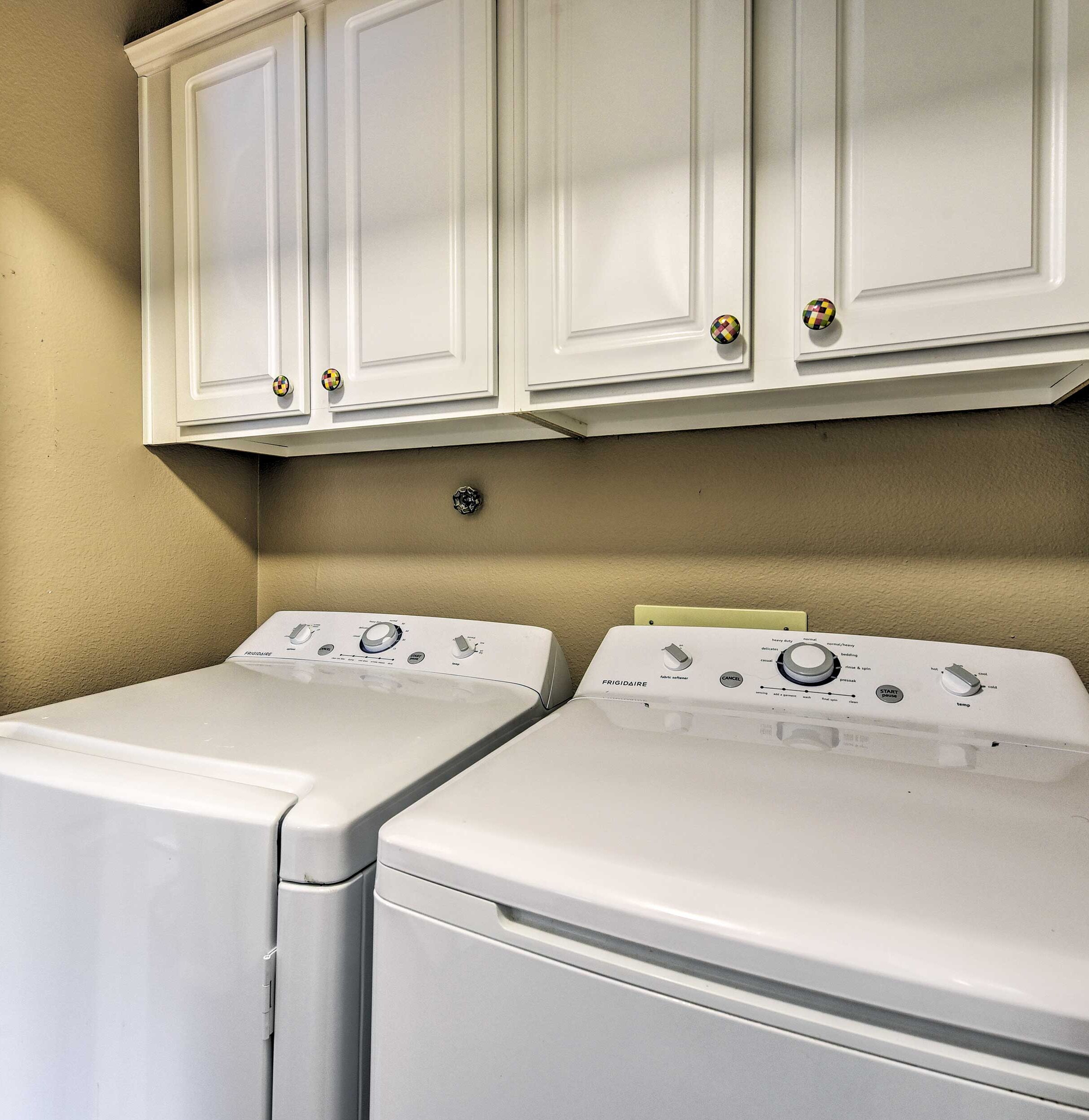 A laundry room with two white front-loading washing machines and white cabinetry above.
