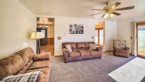 A living room with a brown sofa, a patterned armchair, a ceiling fan, and a large window. - Charming Wisconsin Getaway w/ Nearby Lake! (Pound)