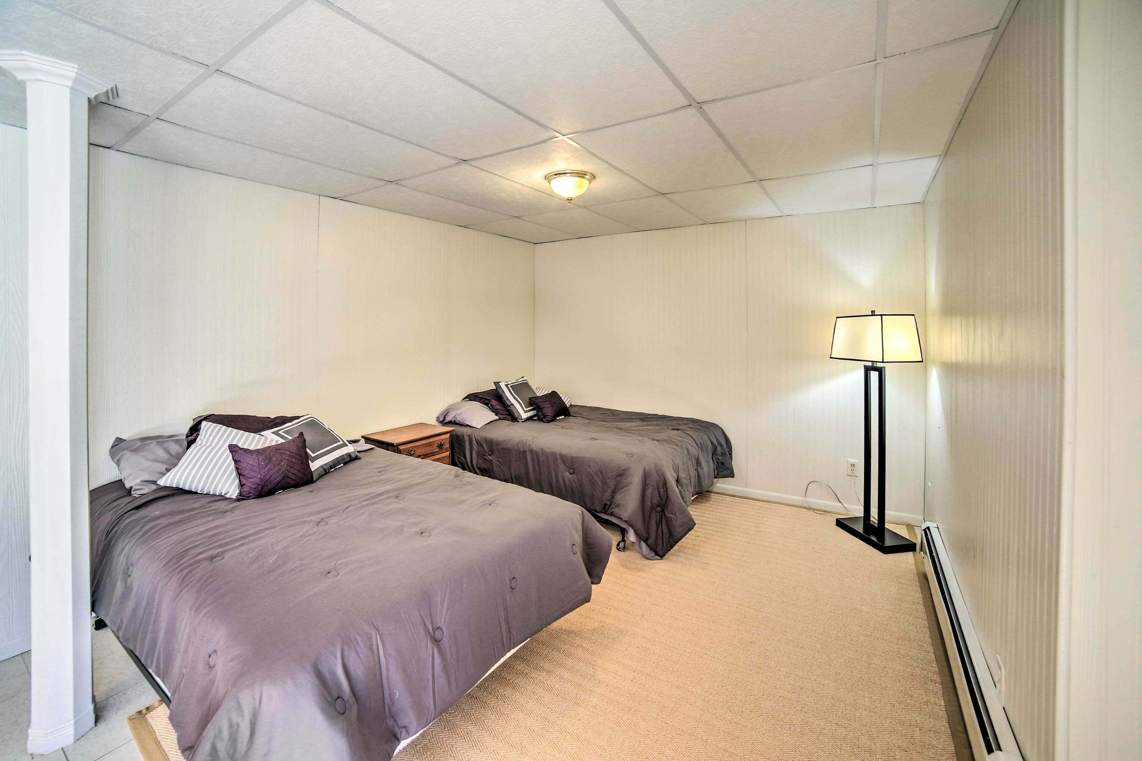 A room with two beds, a nightstand, a lamp, and a ceiling light.