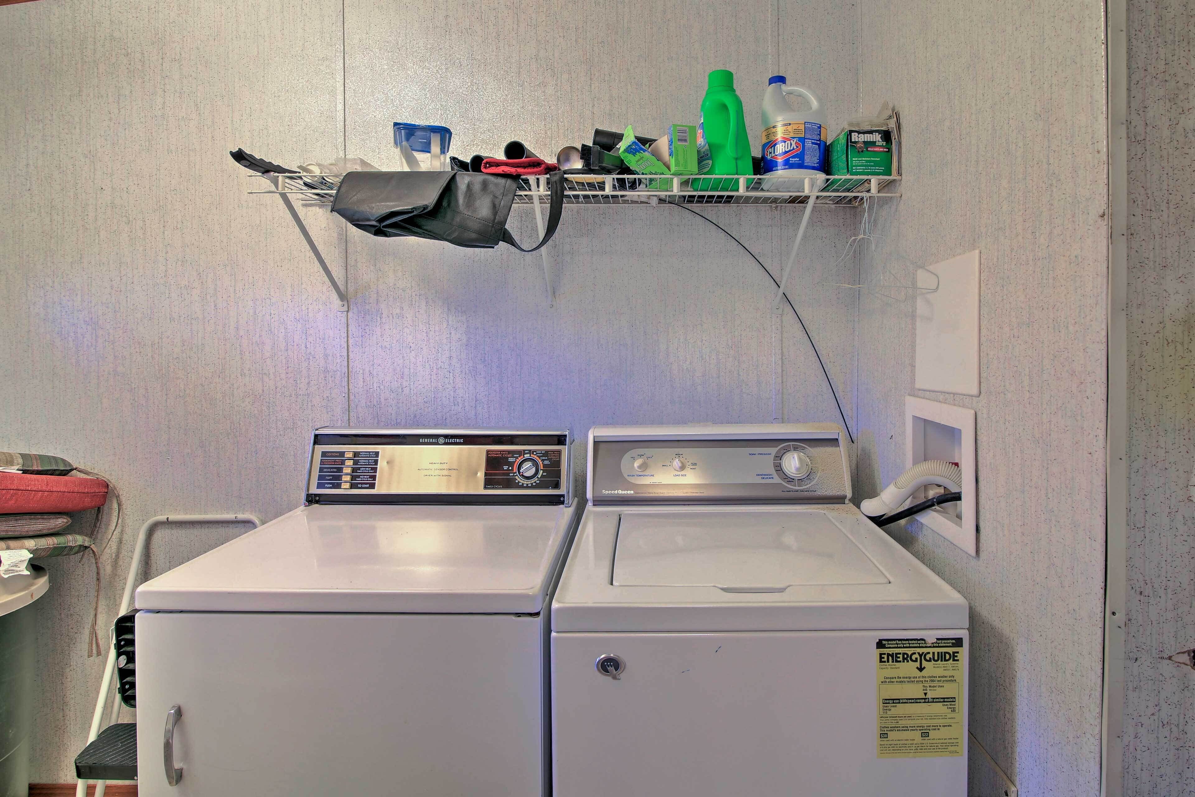 A laundry area with two white washing machines, a shelf with cleaning supplies, and a power outlet.