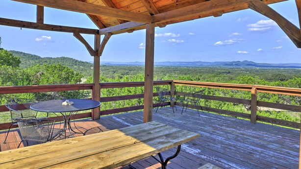 A wooden deck with a table and chairs, overlooking a green landscape with hills. - Spacious Utopia Family Home w/ Hill Country Views (Utopia)