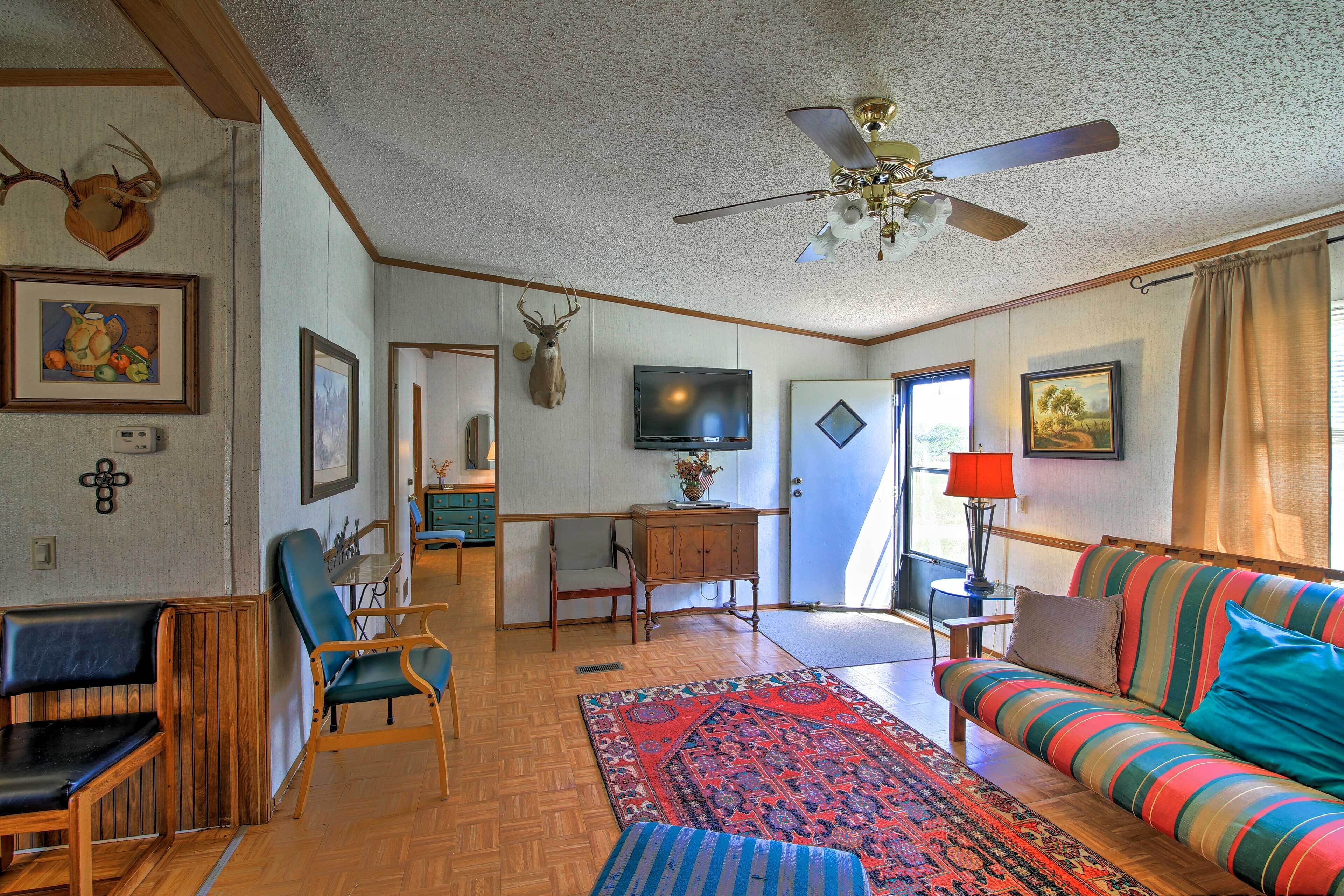 A living room with a sofa, chairs, a television, and a ceiling fan.