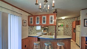 A kitchen with wooden cabinets, a central island with stools, a chandelier, and a refrigerator. - Spacious Utopia Family Home w/ Hill Country Views (Utopia)