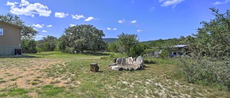 A grassy yard with a stone structure, trees, and a building in the background.