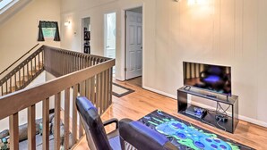A modern living room with a wooden staircase, a flat-screen TV on a glass stand, and a colorful rug. - 7 Mi to Lake Harmony: Home w/ Furnished Deck! (Albrightsville)