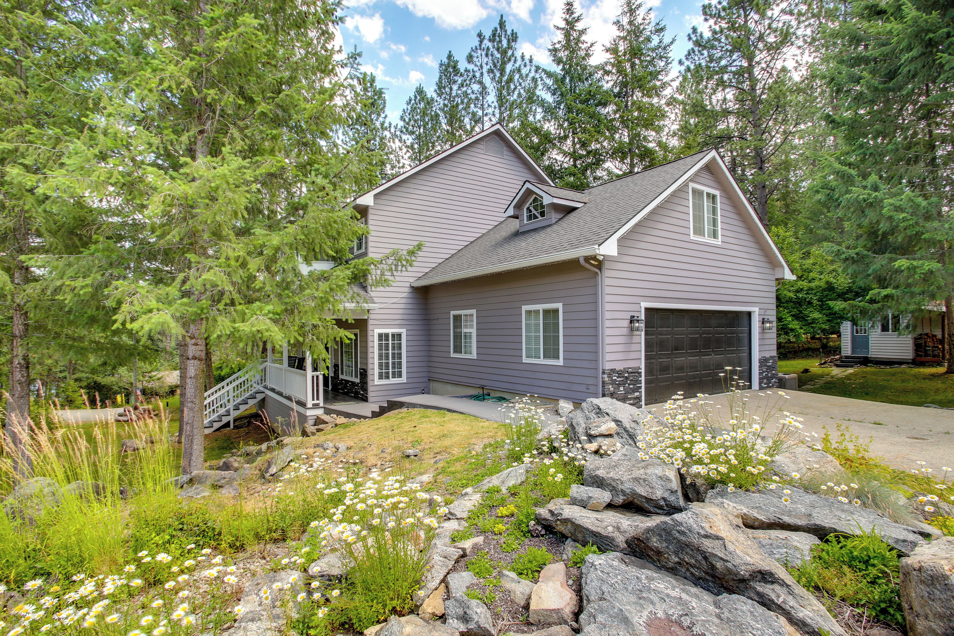 A two-story house with a garage, surrounded by a natural landscape with trees and rocks.