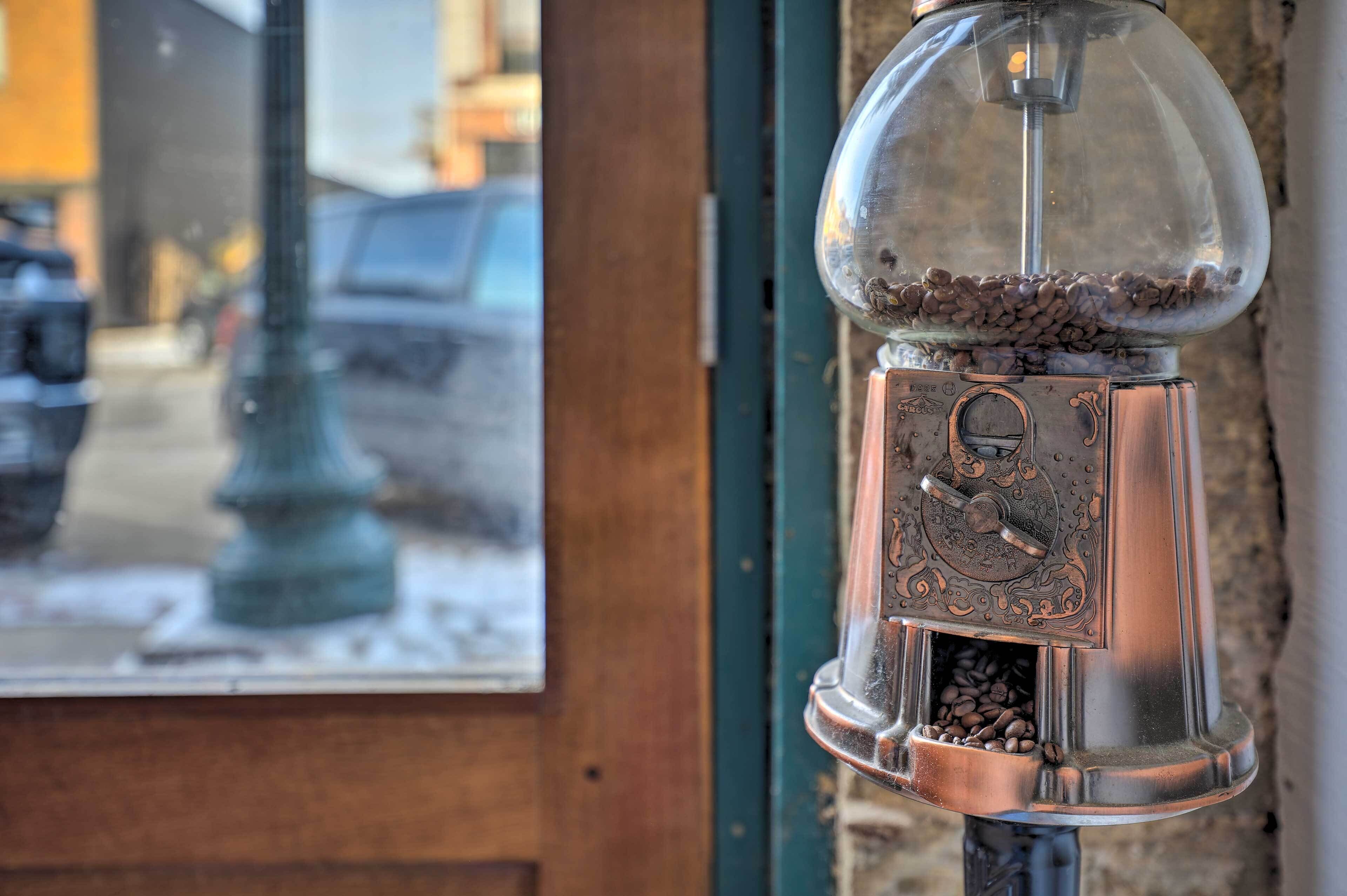 A coffee grinder with a transparent dome, filled with coffee beans, mounted on a wall.