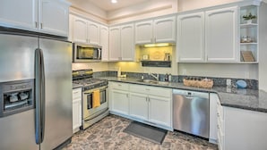 A modern kitchen with white cabinetry, stainless steel appliances, a granite countertop, and a stone backsplash.
