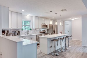 A modern kitchen with white cabinetry, stainless steel appliances, and a central island with bar stools.