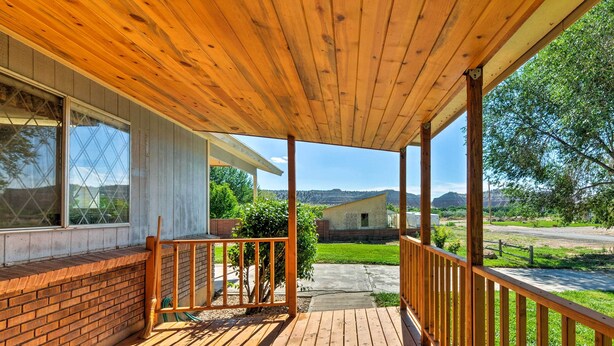 Um deck de madeira com guarda-corpo, uma parede de tijolos e vista para uma casa e paisagem.