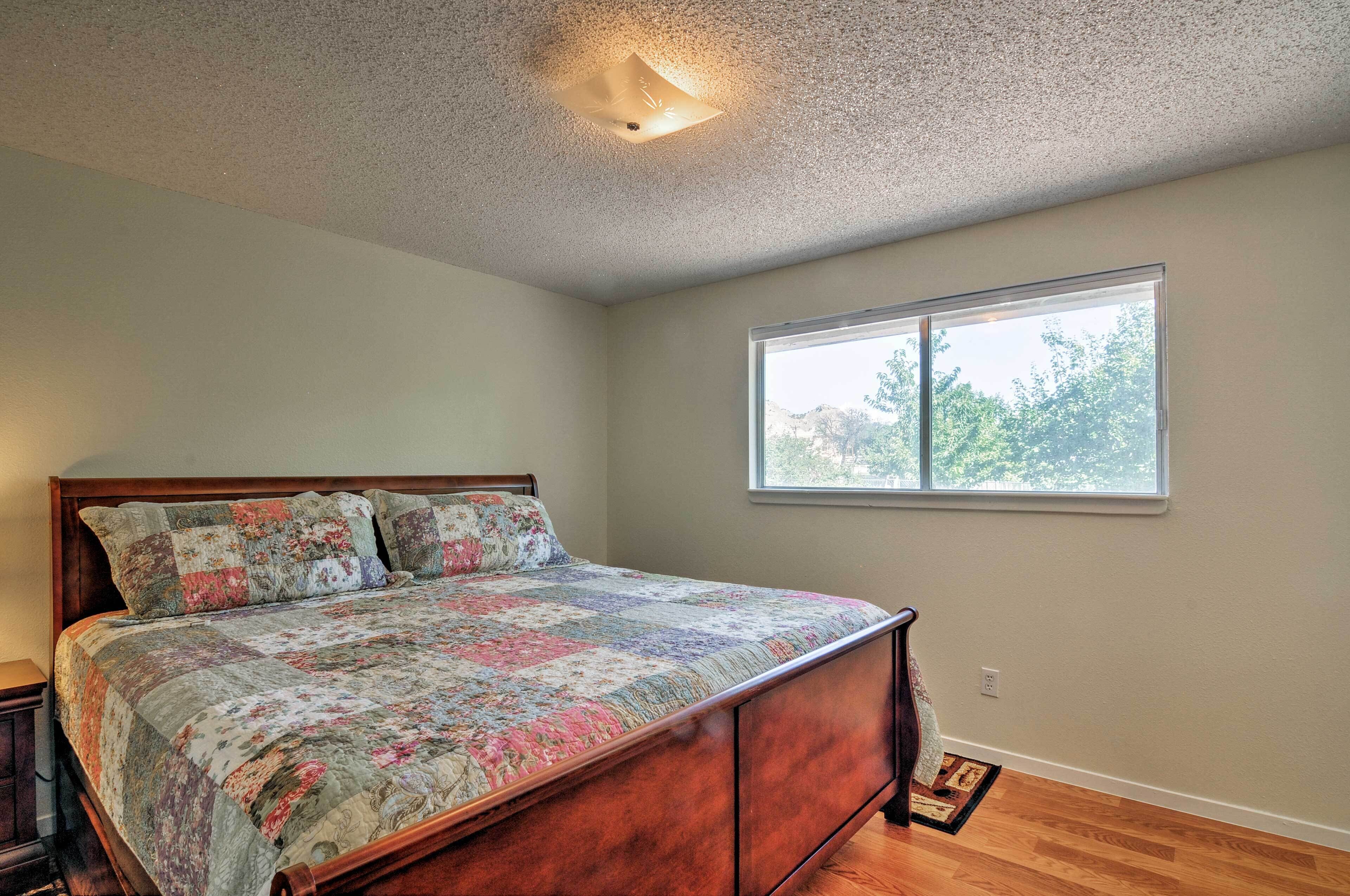 Un dormitorio con cama de madera, ventana con vistas a árboles y una lámpara en el techo.