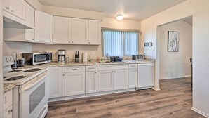 A kitchen with white cabinets, a microwave, a stove, and a window with blinds.