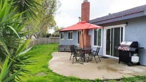 A patio with a table and chairs, a grill, and a red umbrella.