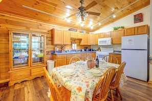 A wooden cabin interior with a dining table set for four, a kitchen with wooden cabinets, a microwave, and a refrigerator. - Cozy Deer Glen' Cabin w/ Private Hot Tub & Porch! (Bryson City)