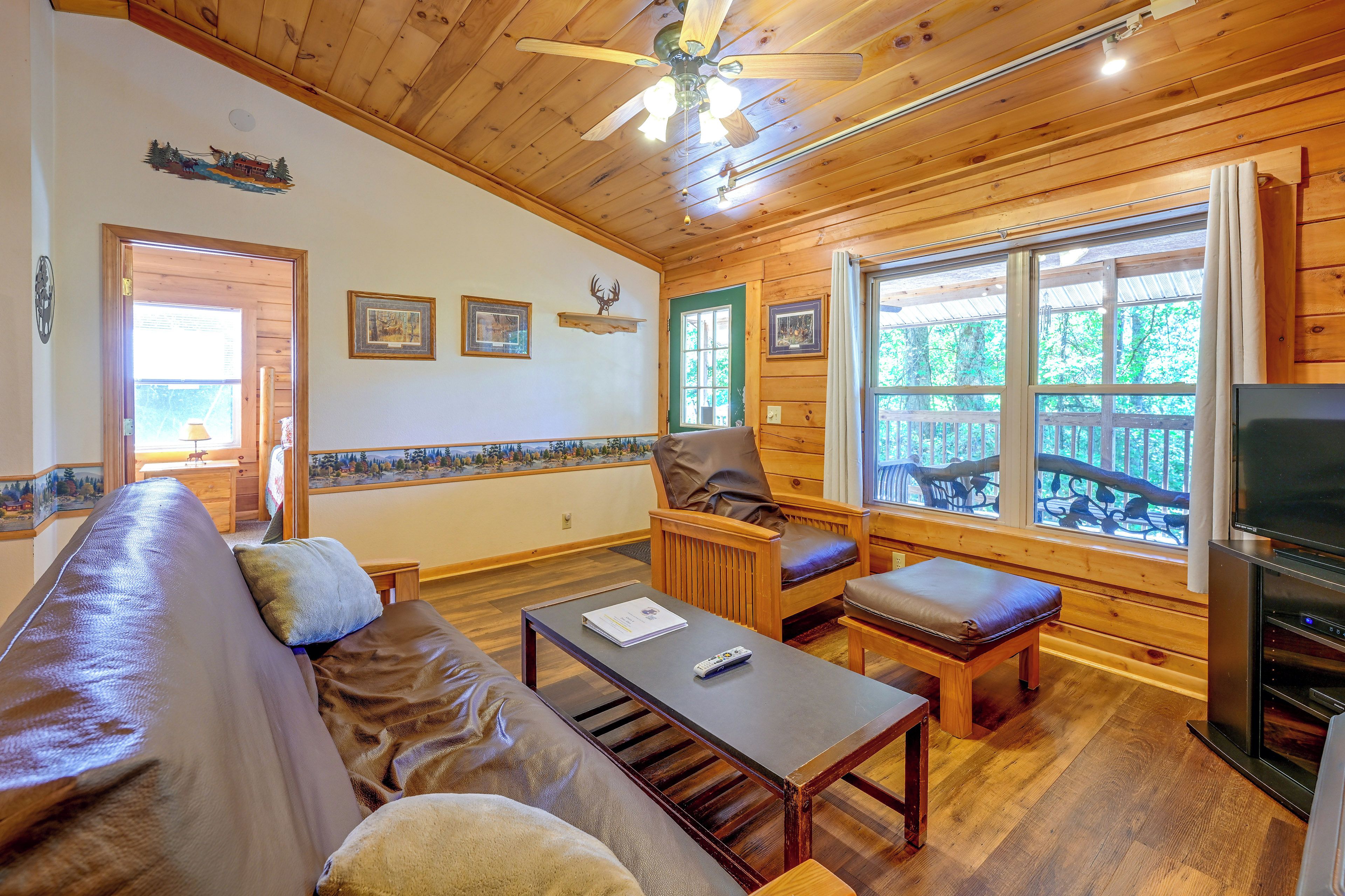 Een gezellig chaletinterieur met een bank, een tafel, een televisie en een balkon met uitzicht op het bos.