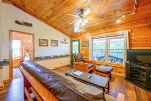 A cozy cabin interior with a wooden ceiling, a ceiling fan, a fireplace, a television, and a bench. - Cozy Deer Glen' Cabin w/ Private Hot Tub & Porch! (Bryson City)