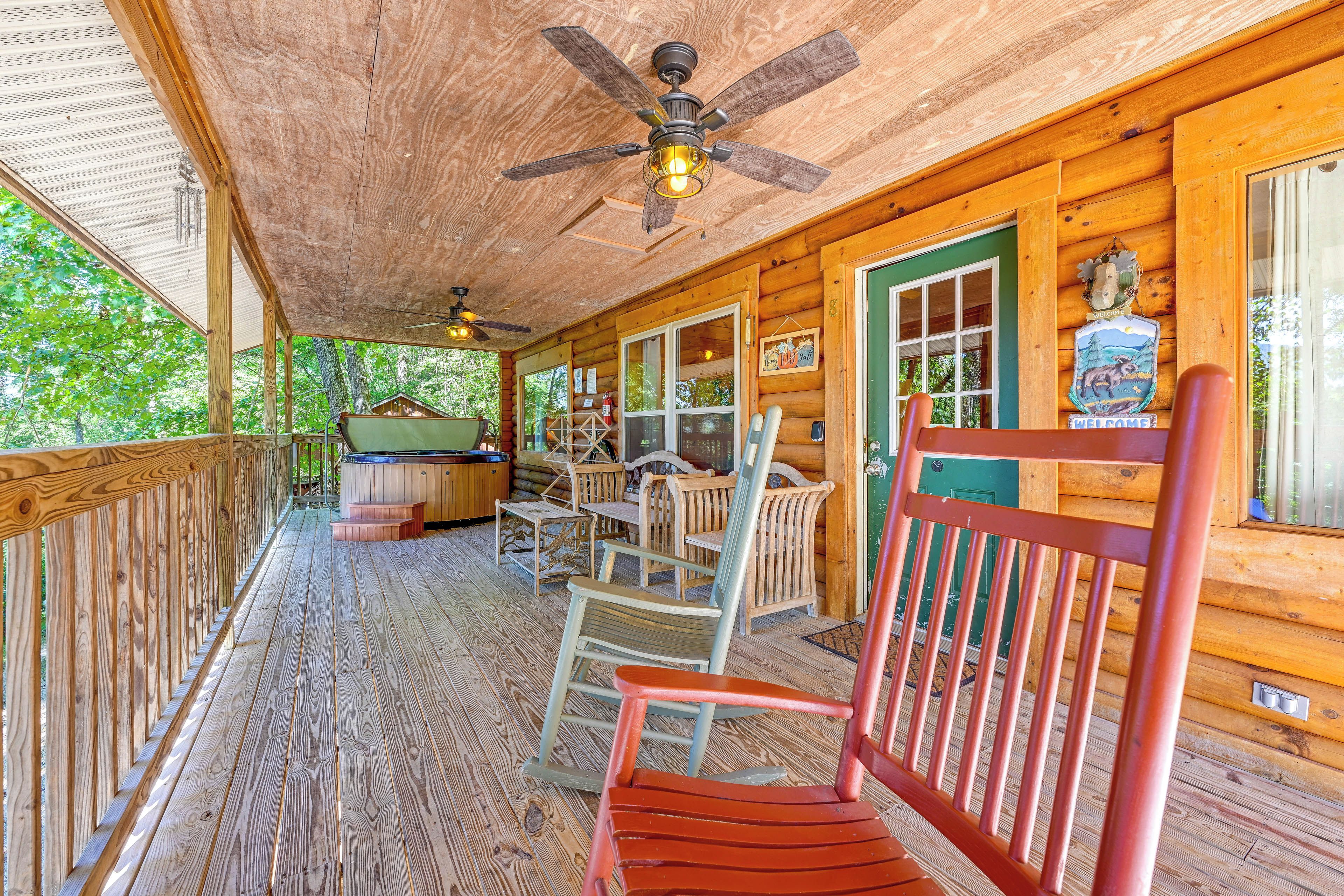 A wooden cabin with a porch, a ceiling fan, and a hot tub.