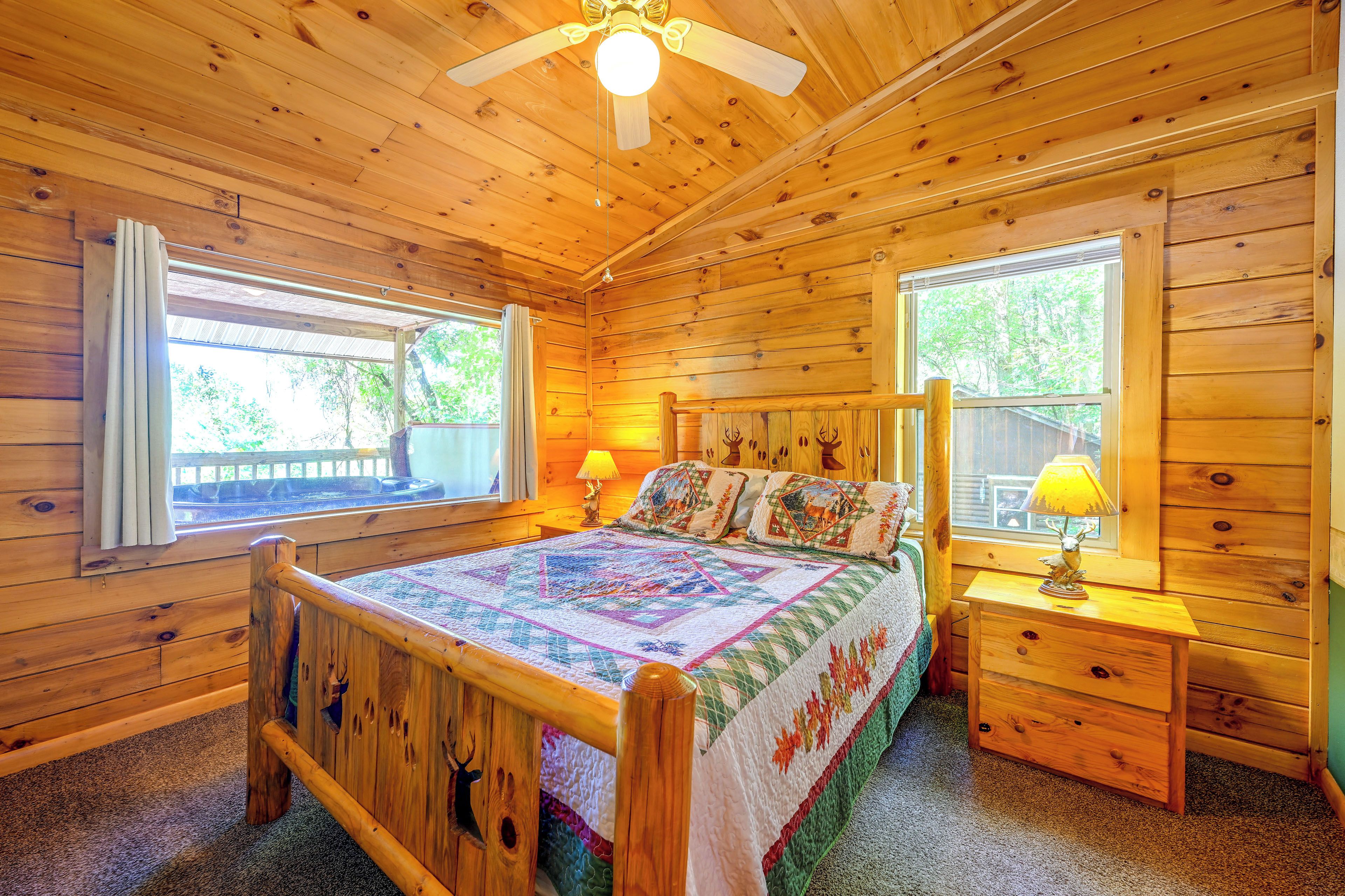 Ein Schlafzimmer in einer Holzhütte mit einem Bett, zwei Fenstern, einem Deckenventilator und einem Nachttisch mit einer Lampe.