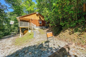 A cabin with a wooden exterior, a balcony, and a gravel driveway leading to a parking area.